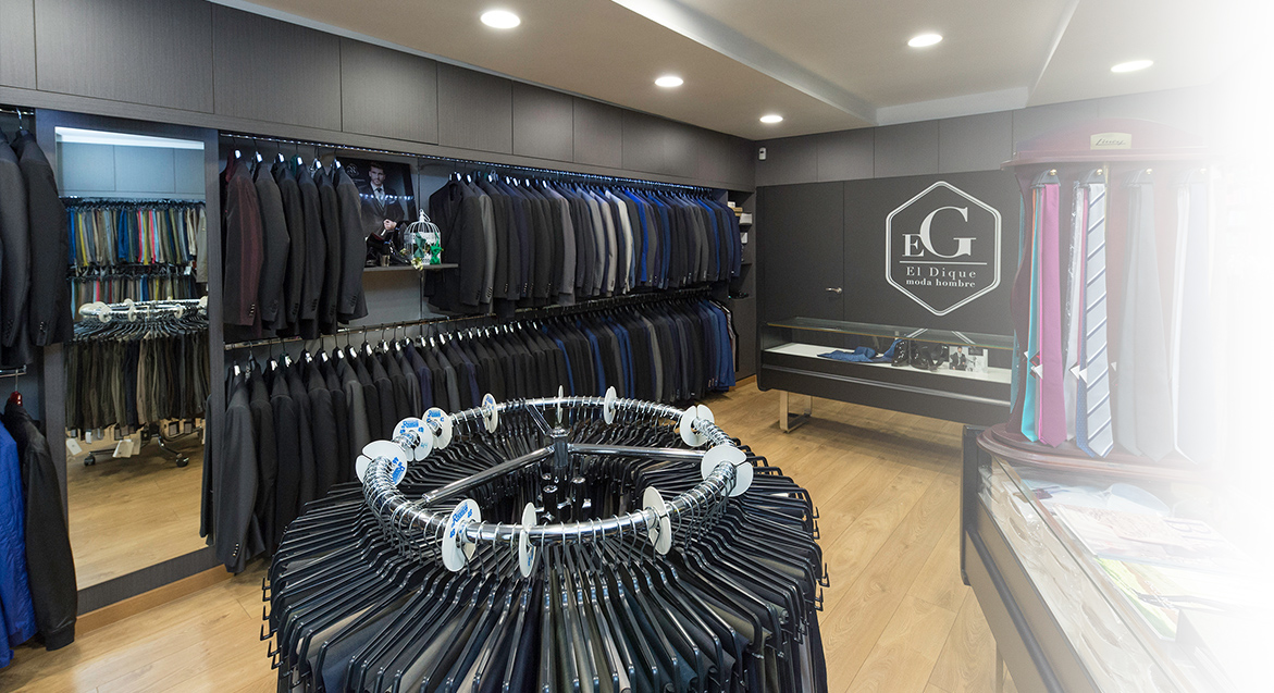 Interior de la tienda de El Dique Moda, tienda de moda para hombre en Ferrol. Interior de color negro y blanco, lleno de trajes para hombre, chaquetas de traje, pantalones de traje y corbatas